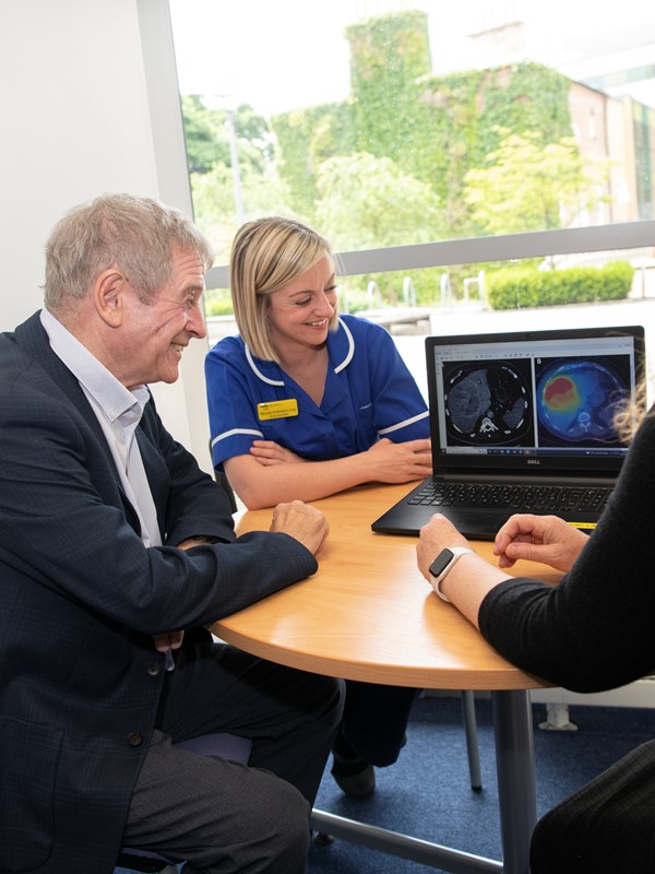A blonde nurse and a grey haired man are looking at a screen that shows medical screen images.