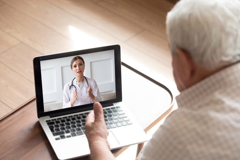 A grey-haired man talks to a nurse via a tablet.