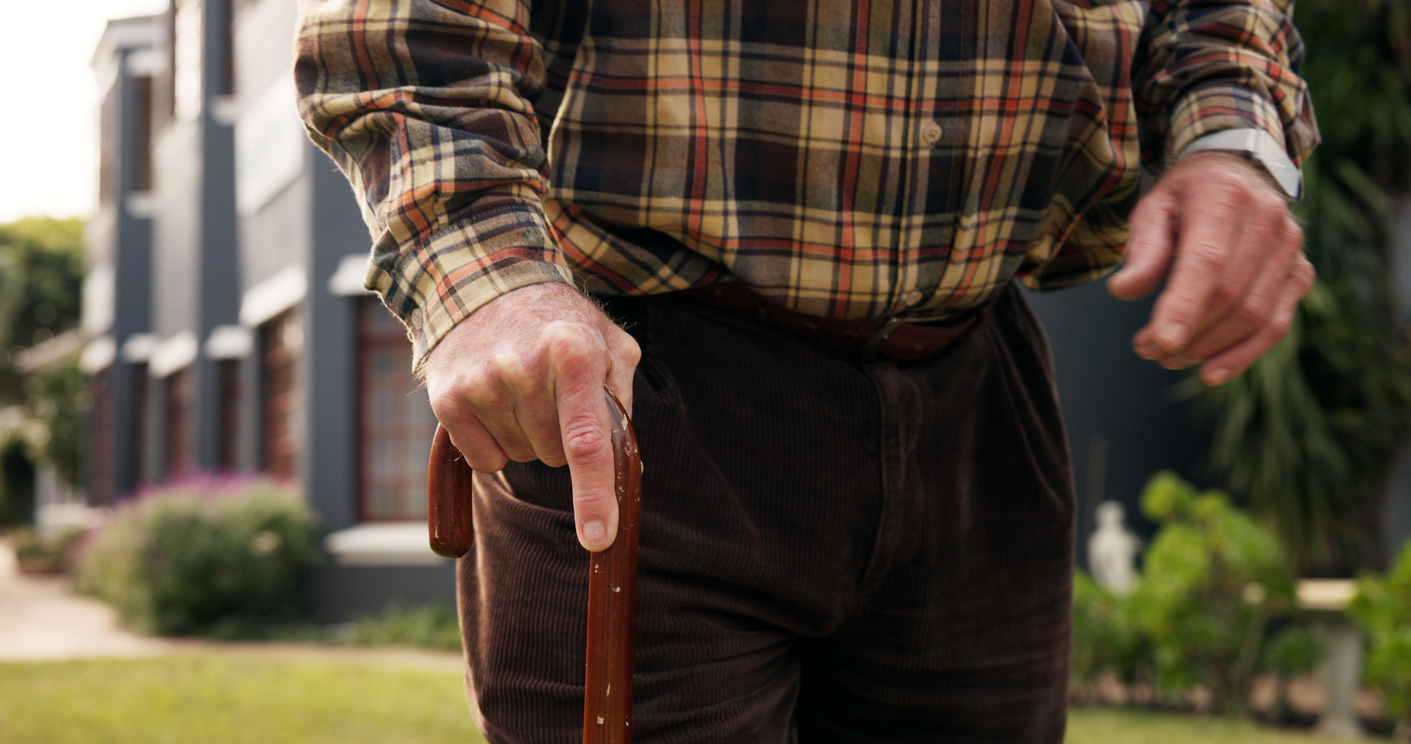 A close up on the hands of a senior person walking with a stick in a garden