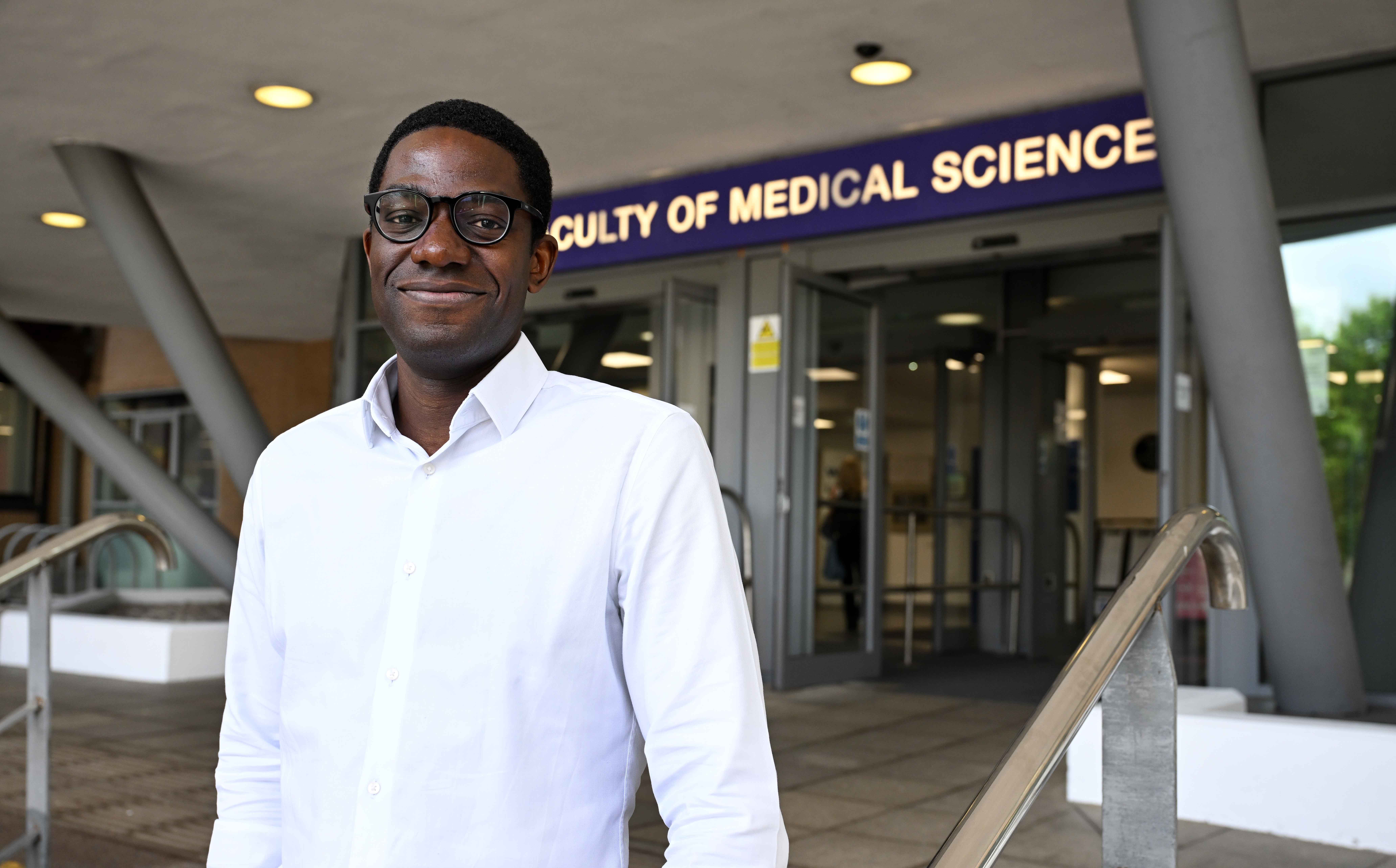 A man is standing in front of the main entrance of the faculty of medical science of Newcastle University